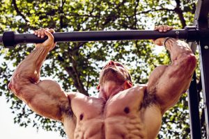 Homme musclé faisant des tractions sur une barre en extérieur