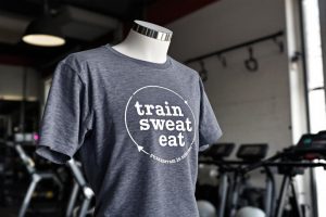 T-shirt gris avec slogan 'train sweat eat' dans un gymnase